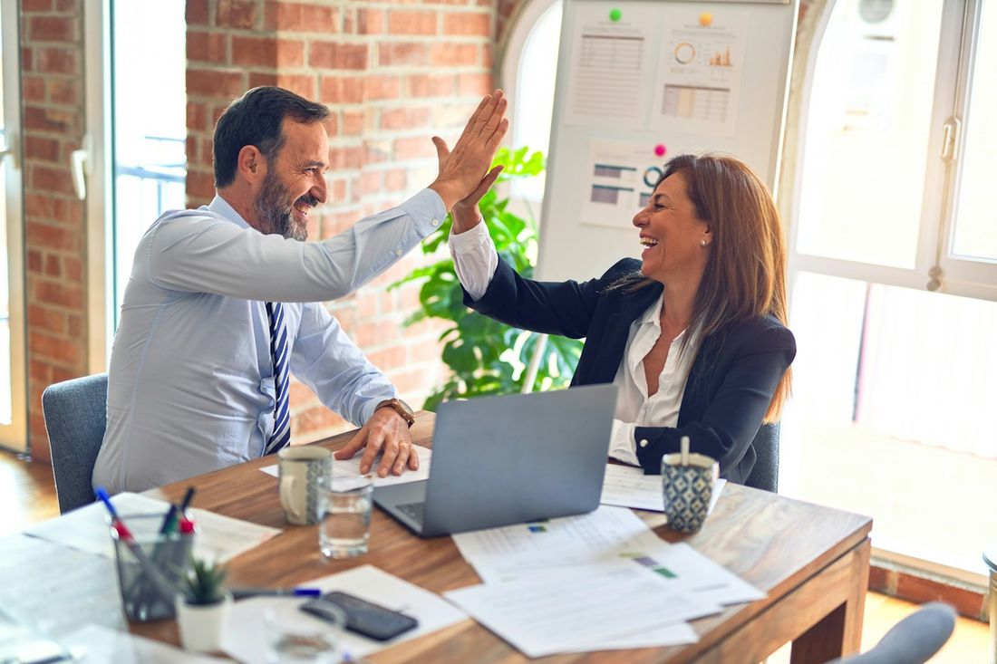 Two colleagues celebrating with a high five at a desk